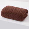 A dark brown, textured bath towel rolled up on a white surface.