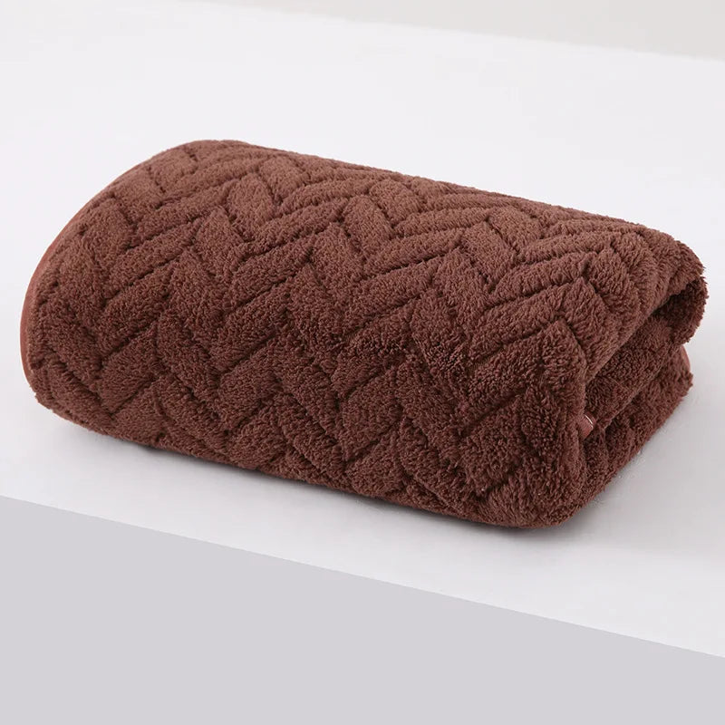 A dark brown, textured bath towel rolled up on a white surface.