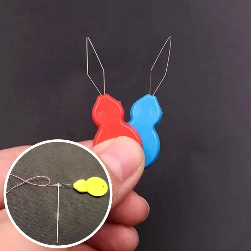 A hand holds a plastic needle threader with red and blue components, showing the tool's function.