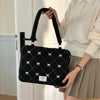 A woman holds a black quilted laptop shoulder bag with a handle and white bow details in a light sweater.