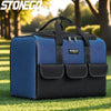 A blue and black heavy duty tool bag with reinforced base and multiple pockets resting on green grass.