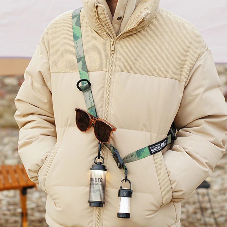A beige quilted jacket features a green patterned strap with a hanging ring and attached sunglasses.