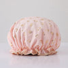 A light pink reusable elastic shower cap adorned with gold heart patterns.