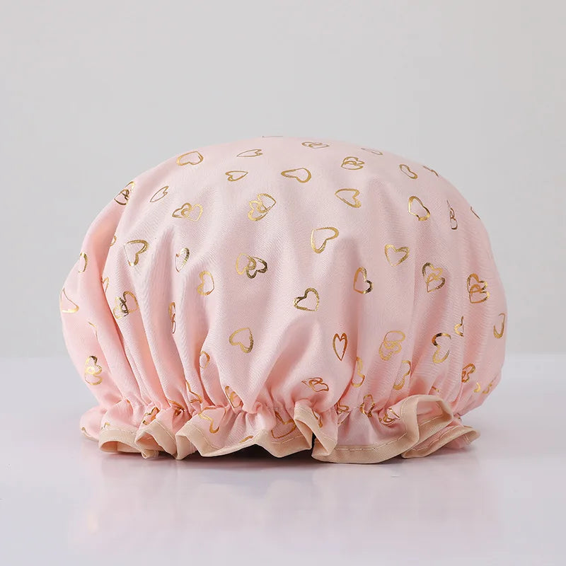 A light pink reusable elastic shower cap adorned with gold heart patterns.