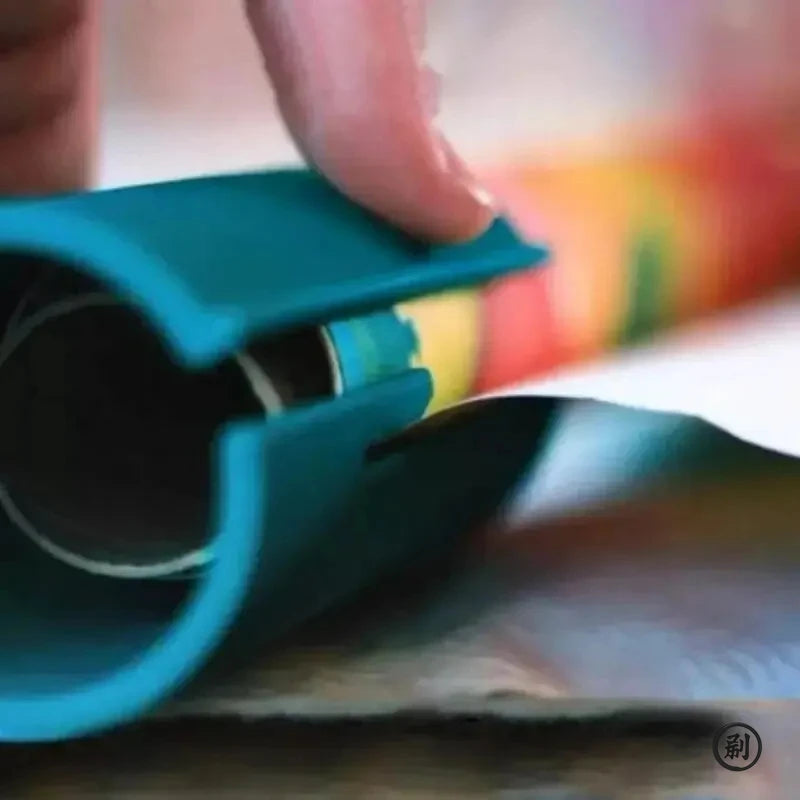 A hand is operating a teal compact safe paper cutter for wrapping and crafts on a surface.