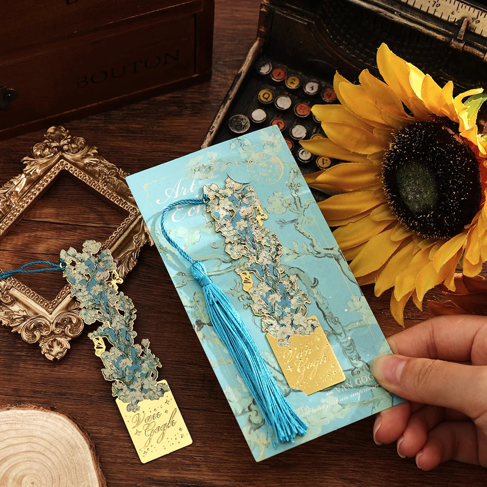 A vintage metal bookmark with an artistic hollow design and blue tassel resting on a light blue patterned card.