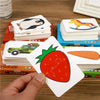 A hand holds a white puzzle card featuring a red strawberry with a green leafy top, placed among stacks of similar cards.