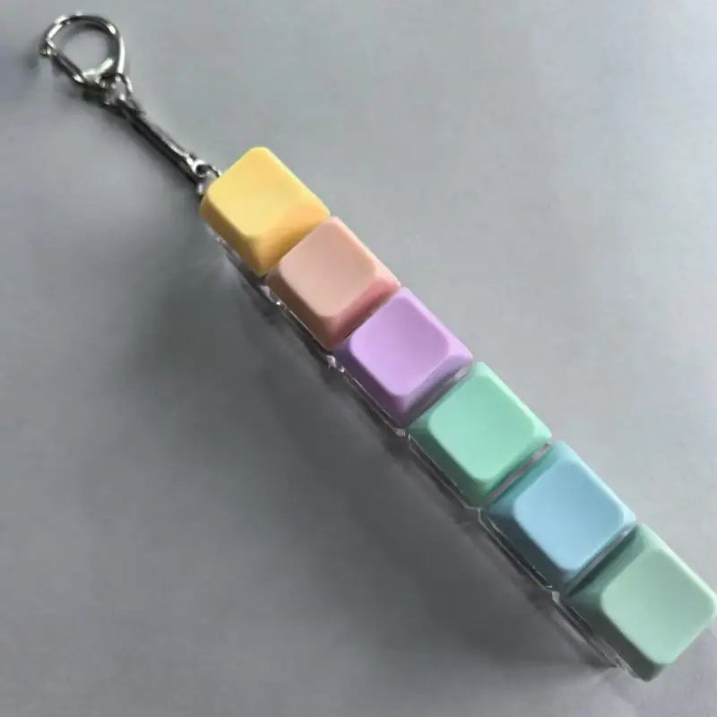 A colorful LED mechanical keychain fidget toy featuring stacked, translucent keycaps in yellow, pink, purple, and mint green.