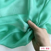 A hand is folding a piece of light mint green silk chiffon fabric.