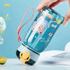 A hand holds a teal cartoon straw water bottle with a yellow leak-proof lid, demonstrating its seal.
