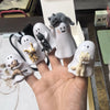 A hand holds several white ceramic figurines of cats and kittens in various poses and sizes.