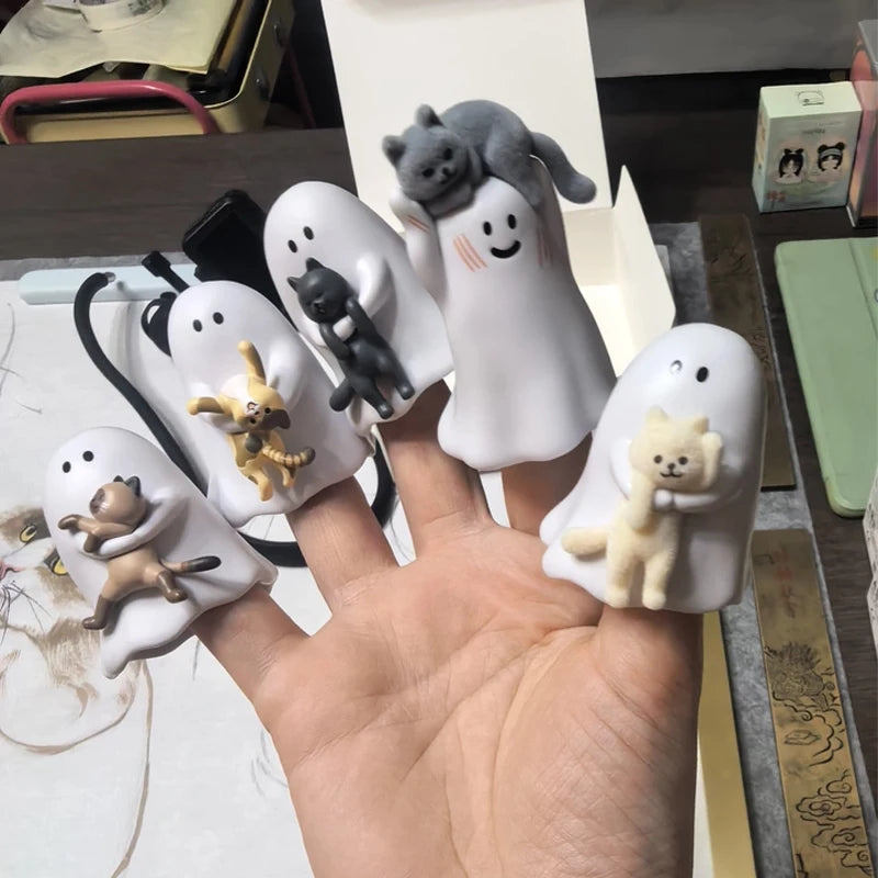 A hand holds several white ceramic figurines of cats and kittens in various poses and sizes.