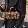 A brown leather mini leopard print hobo satchel bag carried by a person wearing a black coat.