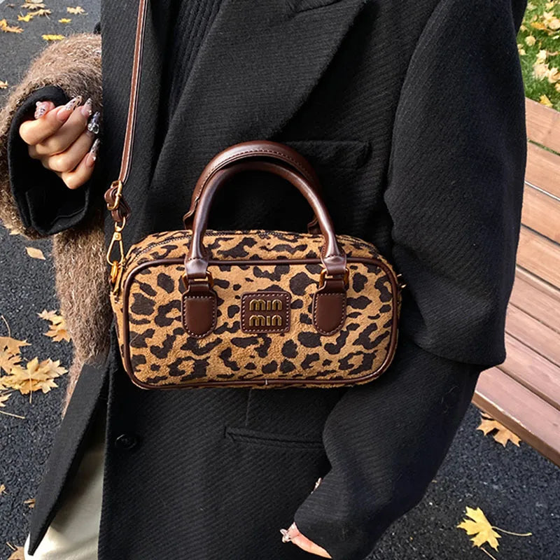 A brown leather mini leopard print hobo satchel bag carried by a person wearing a black coat.