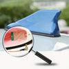 A magnifying glass shows the detail of an aerodynamic shark fin car antenna with a signal amplifier on a blue car surface.