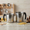 Stainless steel wax melting pitcher and tools with yellow wax pellets on a wooden surface