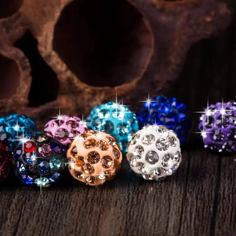 A collection of colorful crystal clay round beads in various shades including blue, purple, pink, and gold resting on a dark 