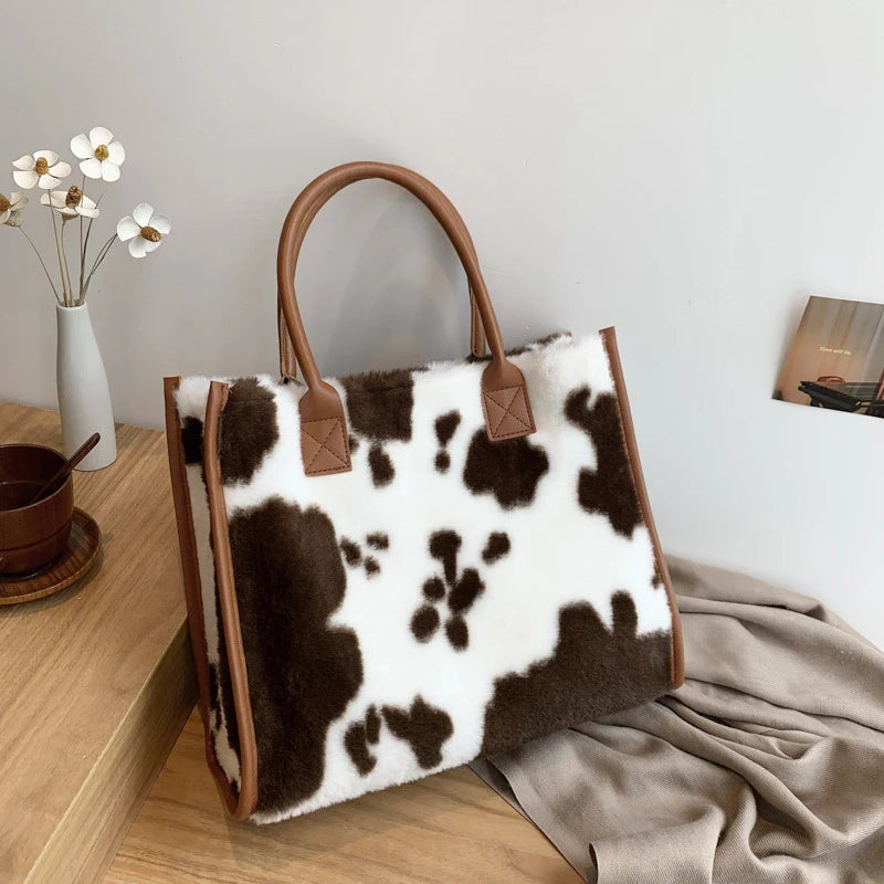 A brown faux fur leopard print tote bag with leather handles resting on a wooden surface.