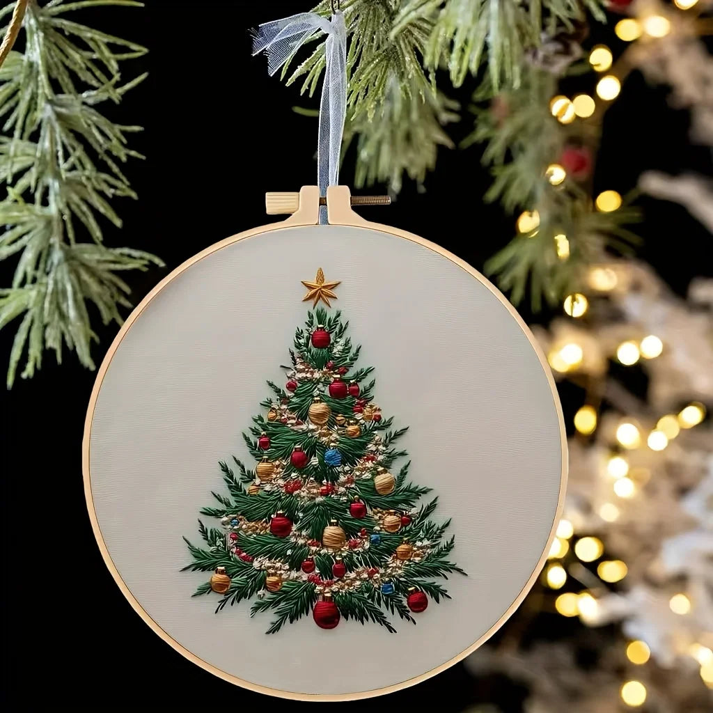 A circular embroidery kit featuring a detailed handcrafted Christmas tree design on a cream fabric, suspended by a twine hang