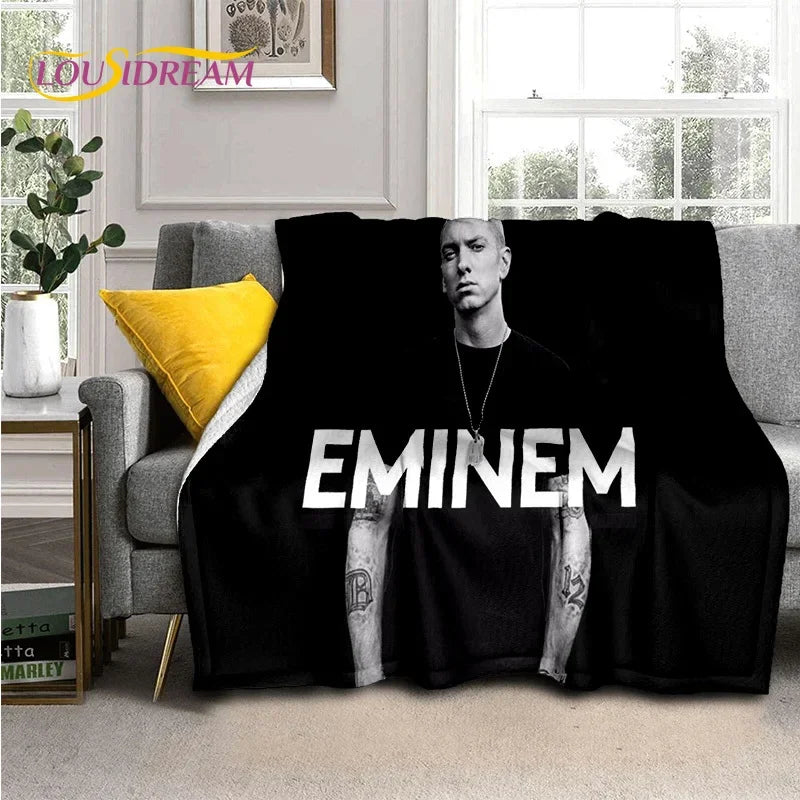 A black throw blanket featuring a portrait of Eminem and 2Pac hip-hop icons draped over a gray sofa.