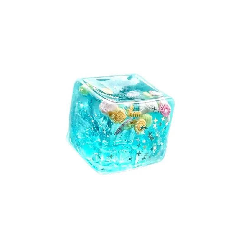 A clear blue, cube-shaped stress relief squeeze toy with glitter and sea life designs.