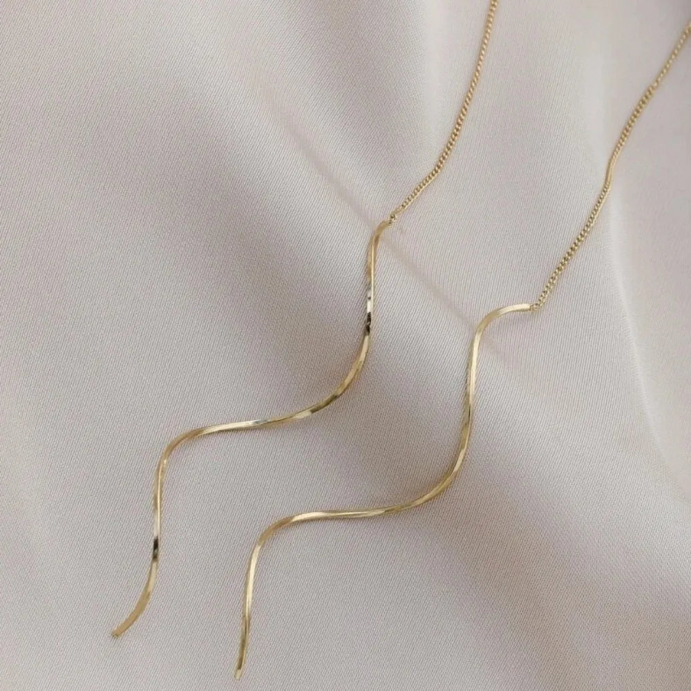 Gold long chain threader earrings displayed against a white fabric background.