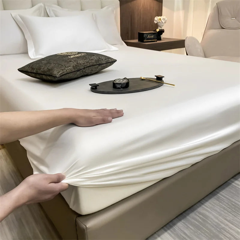 Una mano ajusta una sábana blanca ceñida en una cama con una almohada y accesorios oscuros.