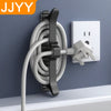 A black cable organizer with an adhesive mount is shown mounted on a gray wall next to a white electrical outlet.