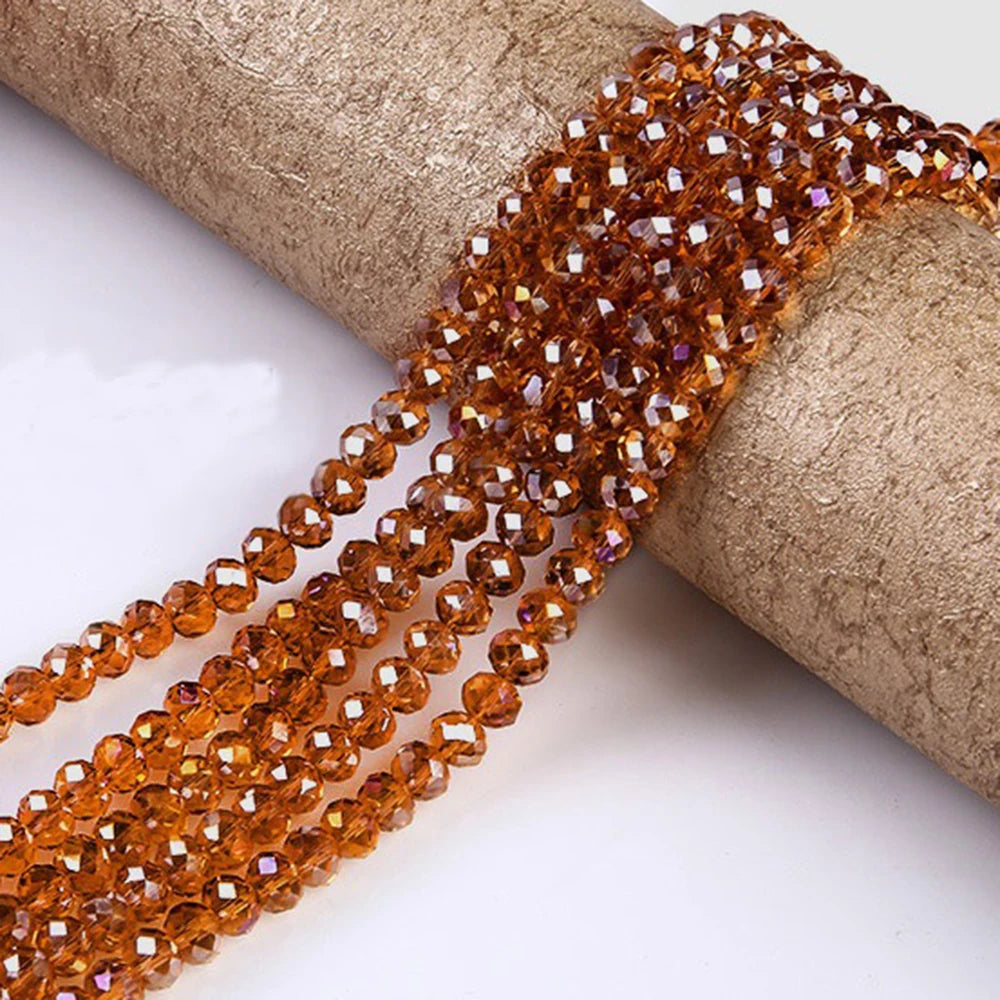 A strand of faceted amber crystal glass spacer beads is laid across a textured beige cylindrical object.