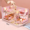 A wooden dollhouse miniature building kit featuring pink furniture and rooms displayed on a light pink background.