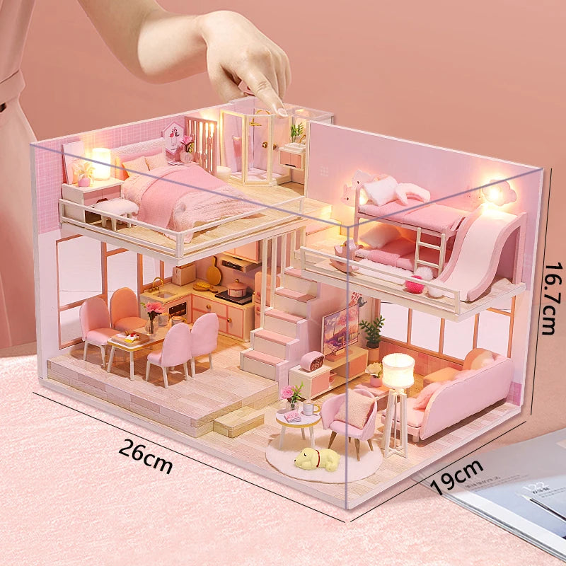 A wooden dollhouse miniature building kit featuring pink furniture and rooms displayed on a light pink background.