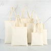 A collection of natural canvas shopping tote bags in off-white and cream colors displayed on a white marble surface.