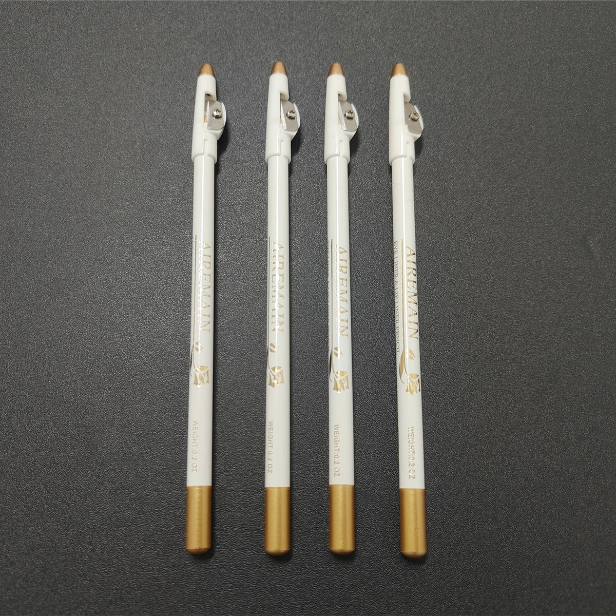 Three precision hairline and beard shaping pencils with gold accents standing vertically on a dark surface.