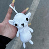 A white plush chihuahua dog keychain pendant is held in a hand against a gray background.