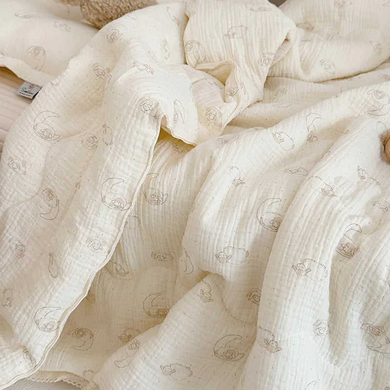 A soft, cream-colored muslin baby blanket with a subtle floral pattern is draped and folded.