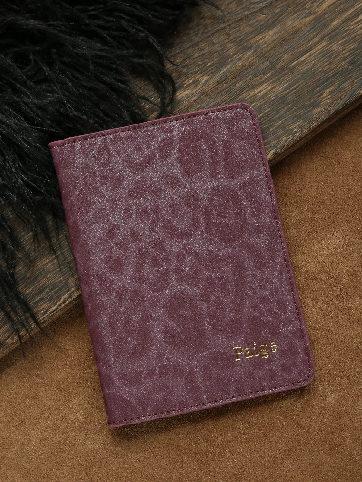 A deep purple leopard print passport holder with gold name embossing resting on a brown surface.
