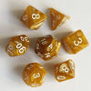 A set of seven translucent amber and yellow polyhedral dice resting on a white surface.