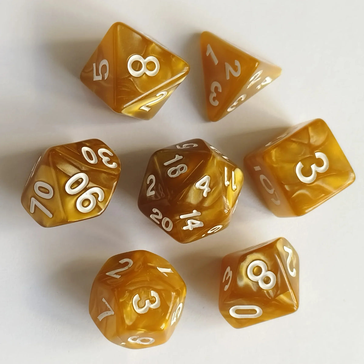 A set of seven translucent amber and yellow polyhedral dice resting on a white surface.
