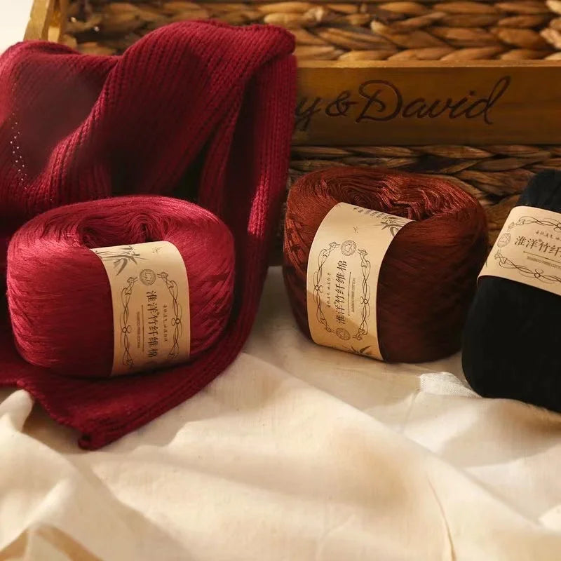A close-up of deep red yarn rolls and knitted fabric displayed on a white surface with a wooden box in the background.