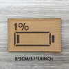A tan fabric patch with black text showing 1% and a cylindrical shape on a wooden surface.