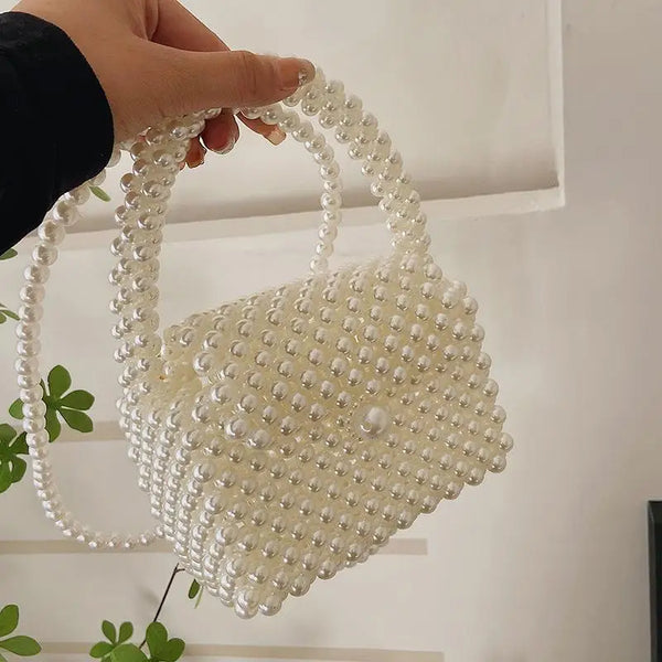 Una mano sostiene un bolso cruz blanco adornado con perlas contra un fondo blanco.