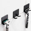 Black aluminum wall-mounted adhesive razor holder with a handle and blade visible on a white tiled surface.