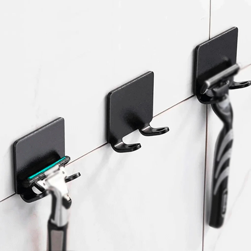 Black aluminum wall-mounted adhesive razor holder with a handle and blade visible on a white tiled surface.