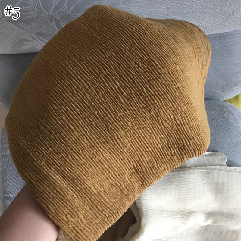 وشاح أو شال من القطن المكركي بلون أصفر خردلي موضوع على سطح رمادي فاتح.