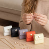 A person is holding a beige sweater and displaying various gold and silver jewelry organizers and pouches on a wooden surface