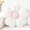 A white plush daisy flower throw pillow with pink center and green stems resting on a white surface.