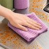 A hand is wiping a stainless steel surface with a purple reusable tear-away cleaning cloth.