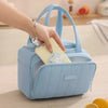A hand is placing a silver necklace into the pocket of a light blue quilted insulated lunch tote bag.