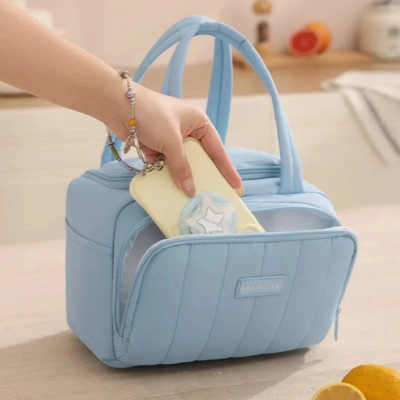 A hand is placing a silver necklace into the pocket of a light blue quilted insulated lunch tote bag.