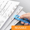 A hand is using a blue reusable push clamp stapler to bind paper documents.
